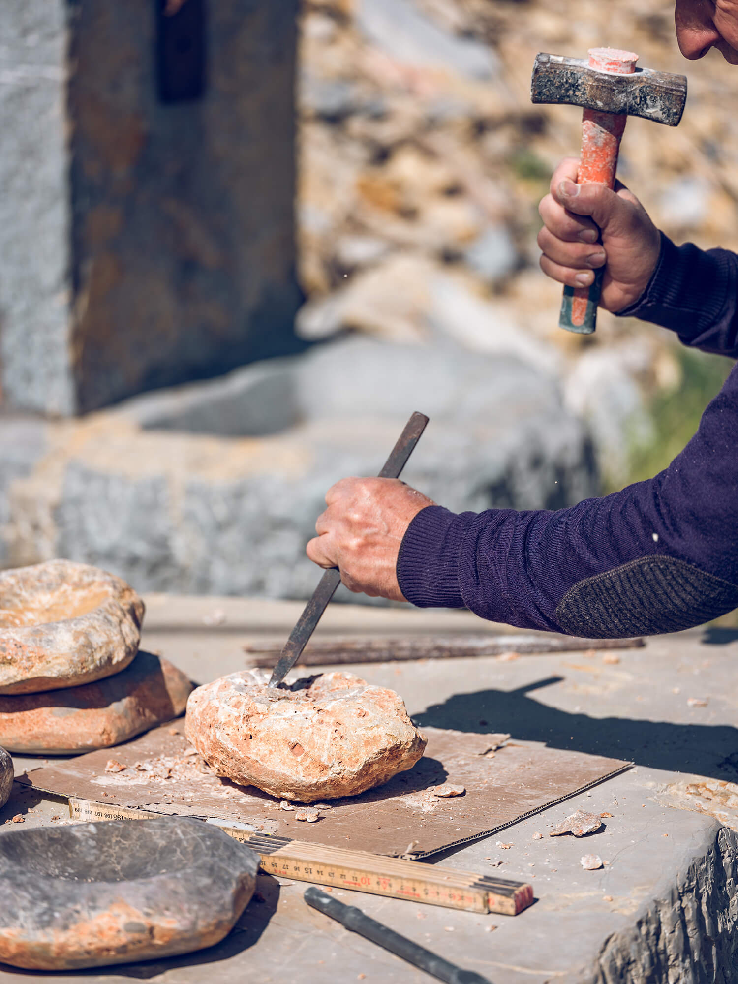 Crop anonymous craftsman cutting rock using chisel and hammer while creating stone craft on workbench in sunny day